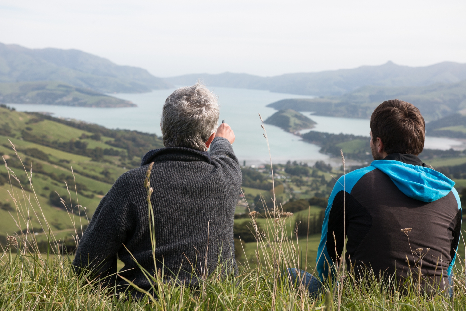 Zwei Männer sitzen auf einem Aussichtspunkt im Gras und schauen auf den See